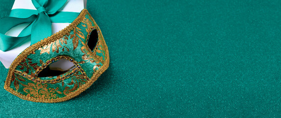 Ornate carnival mask, gift box on glitter trendy green background. Christmas, New year and Mardi gras festive banner with copy space. © Olga