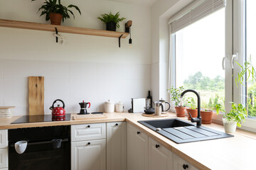Fototapeta na wymiar Interior of kitchen with wooden counter, oven, sink and tap and big window. White kitchen in scandinavian design with minimalism.