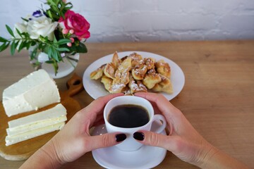 Cup of coffee in female hands, close-up. Homemade baked goods during quarantine. Homemade dessert. Homemade feta cheese on a wooden tabletop. Concept on the background of a white brick wall.