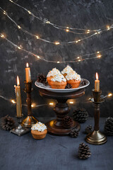 Muffins with butter cream in a vintage plate on a wooden high stand. New Year's festive desserts on the table with a garland and candles.