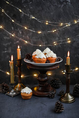 Muffins with butter cream in a vintage plate on a wooden high stand. New Year's festive desserts on the table with a garland and candles.