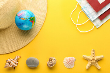 Tourist theme: hat, seashells, starfish, rock, the globe, a medical mask  and foreign passport on a bright yellow background, center space for text. The globe shows South America, North America, USA.