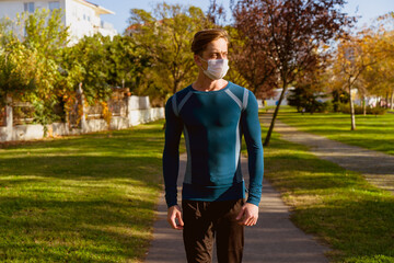 Young man going to the gym with his bag on his shoulder. wearing a protective mask is hiking through the woods. Young male athlete wearing a surgical mask is walking on the jogging track.