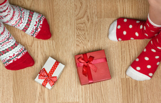 Christmas red socks on wooden floor. Two pairs of feet, dressed in Xmas socks, stand near presents. Concept of happy family at home
