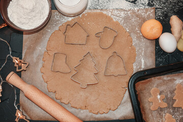 Cooking Christmas gingerbread cookies on a dark background. Cut gingerbread out of the dough using a gingerbread mold, top view, raw dough with cinnamon prepared for baking.