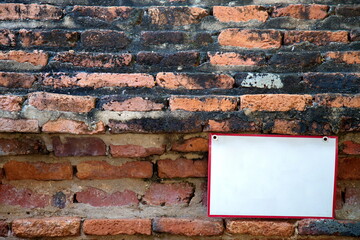 Old red brick wall Full of moss stains There is a white sign with a red border placed in the lower right corner.