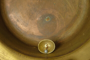 The middle of a gold metal bell with a round tongue. The bell lies on a copper surface. Metal texture. Copy space. 
