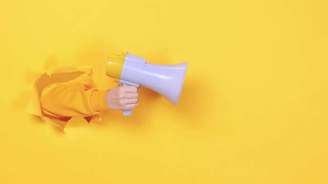 Woman hand arm hold megaphone isolated through torn yellow background Copy space advertisement place for text or image workspace mock up Hot news announce discounts sale hurry up communication concept