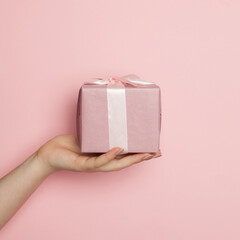 Pink gift box. Minimal background composition with woman hand holding gift on pastel pink color