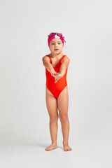 little child girl in swimsuit, swimming goggles and swim cap is preparing for swimmin. Full length. child dreams of becoming a swimming champion