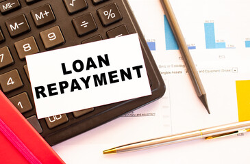 Text LOAN REPAYMENT on white card with metal pen, calculator and financial charts.