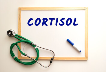 The text CORTISOL is written on a white office board. Nearby is a stethoscope.