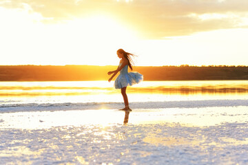 Young ballerina in the sunset light in the water of the lake. Silhouette of a young ballerina in a...