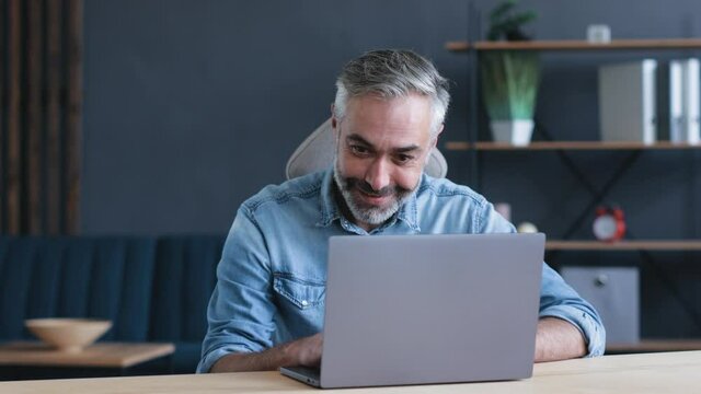 Excited mature Man Winner holding using Laptop, working Home. Male feels overjoyed with Success while working distantly, happy caucasian Man euphoric smiles, celebrates good news victory Success.