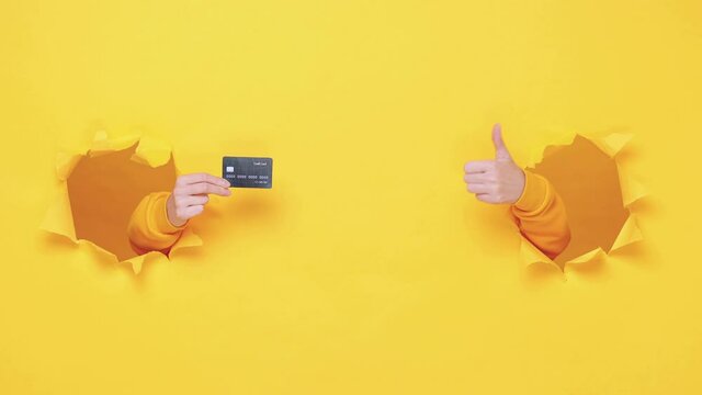 Woman hand arm hold credit bank card isolated through torn yellow wall orange background studio. Copy space advertisement place for text or image promotional content Advertising area workspace mock up