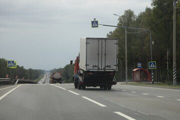 Car carrier truck with broken truck on board drive onsuburban highway road, rear side wide view, delivery autos logistics, automobile transportation