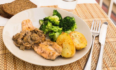 fried river trout fillet with a complex side dish of broccoli, baked potatoes and mushroom sauce