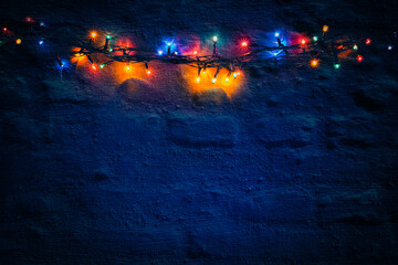 Glowing Christmas tree garland against a dark blue brick wall. Copy space. Christmas background.