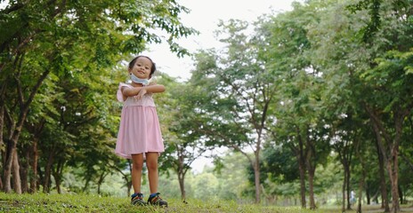 Cute little Asian girl in a pink dress is standing on the grass in a green park , concept of healthy kid life. with copy space

