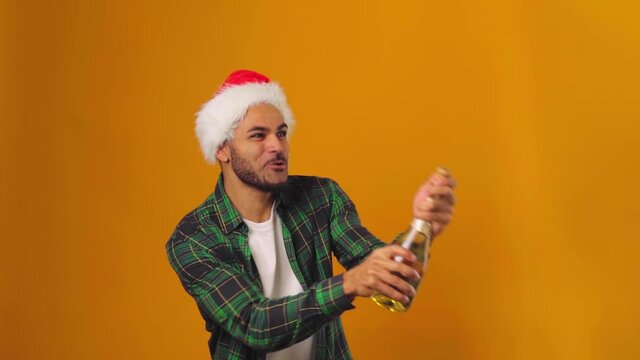 African american man in Santa hat opening champagne bottle with explosion against yellow background