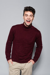  young man in burgundy turtleneck jumper posing isolated on grey