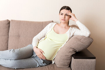 Young pregnant woman with headache sitting on sofa. Pregnancy expectation concept