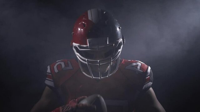 Masculine determined professional American football player in helmet in bright stadium illumination lights ready for game. Confident man in uniform. Usa team game and extreme sport spirit concept.