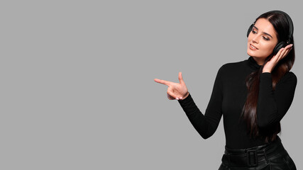 Millennial hipster girl enjoys music podcast in headphones points fore finger on copy space for...