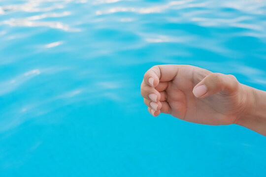 Closeup view horizontal photography of 1 female hand forming gesture as if holding virtual invisible object in palm isolated on bright blue pool water bokeh background.