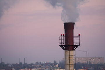 The chimney of the plant, from which puffs of gray-blue smoke emerge, against the background of a...
