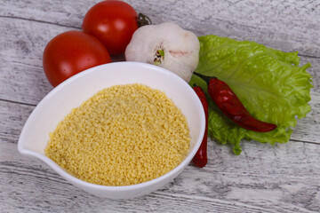 Raw couscous in the bowl served salad leaves, tomato and pepper