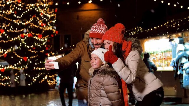 winter holidays, celebration and technology concept - happy family taking selfie with smartphone at christmas market on town hall square in tallinn, estonia