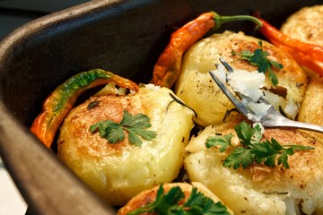 Baked potato with parsley, rosemary, spice peppers on a baking sheet