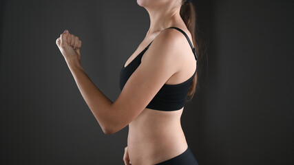 Girl shows her strength strains her hand and clenches her fist. Cropped female body in black underwear. Isolated on gray