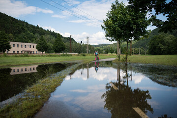 Fototapeta premium Young athlete woman riding a bicycle on a road through the water.
