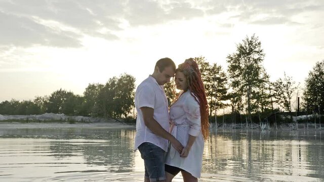 Lake at sunset. Couple of lovers are standing holding hands in the water.