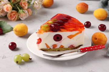 Slice of delicious jelly cake with fruits and berries on a plate on a gray background. Closeup. Horizontal format