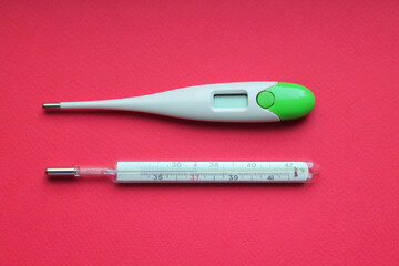 Mercury glass and white electric thermometers are in numbers and screen up. Close-up, top view. Thermometers lie parallel to each other on a bright red surface. Treatment. Medicines.