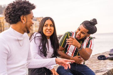 Lifestyle, three black friends smiling a lot in the city with the sunset in the background, slimming and millennial in the city. Afro hair boy, brunette boy with long hair and brunette girl