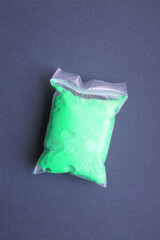 One zip bag with silicone plasticine on a black background, close-up, top view. Plasticine in green color. Transparent zip package. Stationery. Creation. Development.
