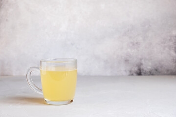 Delicious homemade chicken broth in a glass cup on a light gray background.