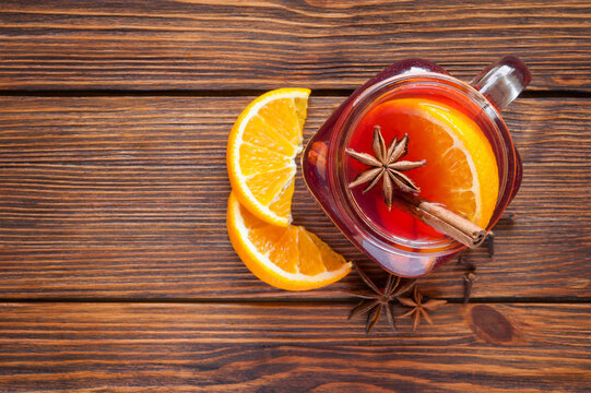 mulled wine in a glass mug on a wooden table top view. warming winter drink with orange wedges and cinnamon