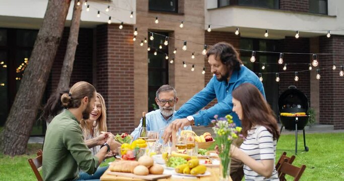 Caucasian happy family of parents, grandparents and kids spending weekend together at back yard outdoor. Cheerful people of different ages having dinner barbecue outside Children playing on background