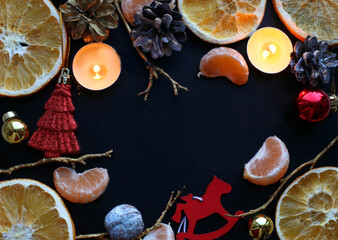 Christmas or New Year frame of dry orange slices, burning candles, cones, golden branches, balls and red ornaments on dark background. Space for text. Top view, flat lay.