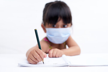 Close-up little girl hand writing in notebook, Wearing a protective face mask