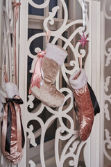 beautiful Christmas socks for gifts with pink and gold color with satin ribbons hang on a white openwork screen near the window                               