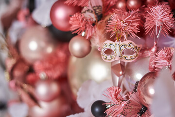 Christmas toy on a pink Christmas tree in the form of a beautiful masquerade mask against the background of other Christmas balls decorating the Christmas tree