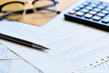 Silver pen on a pile papers with calculator and eyeglasses is background.