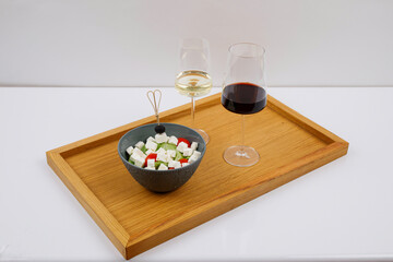 Drewniana taca z lampkami wina czerwonym i białym obok w miseczce kostki sera z warzywami, całośc na białym tle © JDziedzic