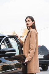 Fototapeta na wymiar woman in stylish trench coat looking away while opening car door